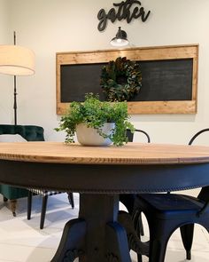 a wooden table topped with a potted plant next to a chalkboard on the wall