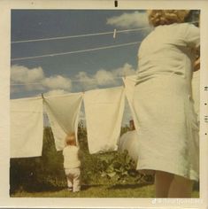 an old photo of a baby standing in front of some clothes hanging on a line