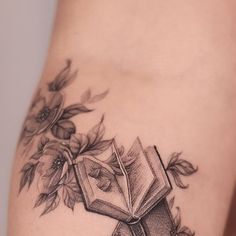 a tattoo with an open book and flowers on it