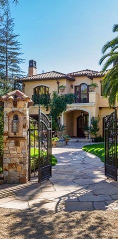 an entrance to a large home with stone pillars and wrought iron gates, surrounded by palm trees