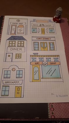 an open notebook with drawings of shops and buildings on the pages, next to a rubber stamp