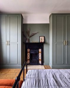 a bedroom with green painted walls and an orange chair in the foreground, next to a fireplace