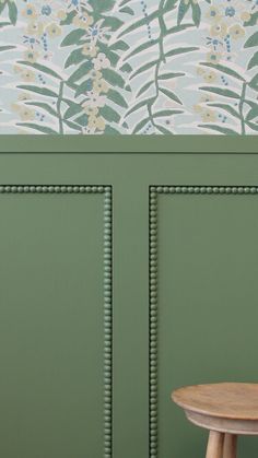 a wooden stool sitting in front of a green wall with flowers painted on the walls