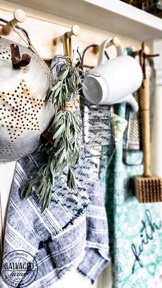 kitchen utensils hanging on the wall next to towels and teapots with rosemary sprigs