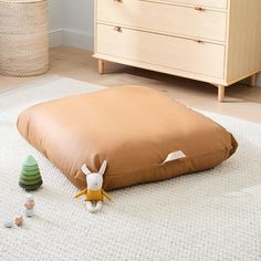 a stuffed animal sitting on the floor next to a brown pillow and toy animals in front of a dresser