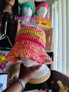 a woman's hand holding up a pink and green crocheted sun hat