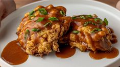 two pieces of fried chicken covered in gravy on a white plate