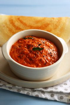 a white bowl filled with red sauce on top of a plate next to some bread