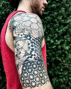 a man with a tattoo on his arm standing in front of some bushes and trees