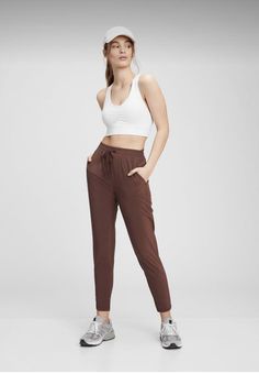 a woman in white top and brown pants with her hands on her hips, looking at the camera