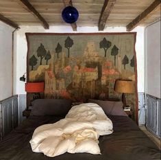 an unmade bed in a room with a tapestry on the wall and two lamps