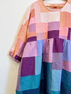 a colorful dress hanging up against a wall with a wooden hanger on it's side