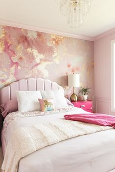 a pink and gold bedroom with white bedding, chandelier and pillows on the headboard