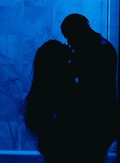 a man and woman standing next to each other in front of a blue wall,