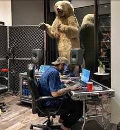 a man sitting at a desk in front of a large bear statue on top of a laptop computer