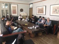 a group of people sitting around a wooden table in a room with pictures on the wall