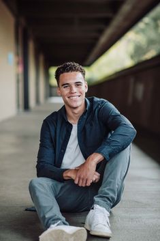 a man sitting on the ground with his legs crossed and smiling at the camera,