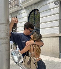 a man and woman hugging each other on the street next to a metal pole in front of a building