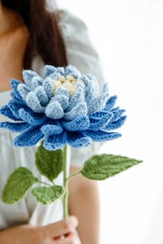 a woman holding a crocheted blue flower in her right hand and wearing a white shirt