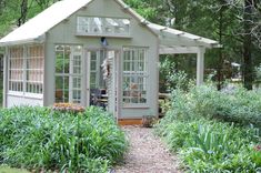 a small green house surrounded by greenery and trees