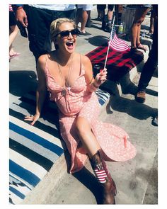 a woman sitting on the ground holding an american flag in her right hand and smiling