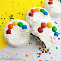 three decorated cookies with white frosting and multicolored candies on yellow background