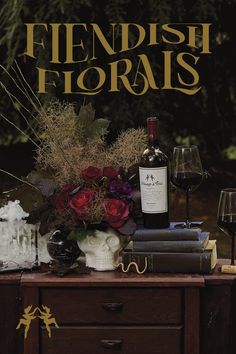 a table topped with lots of books and wine glasses next to a vase filled with flowers