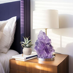 a nightstand with a lamp and a purple rock on it in front of a bed