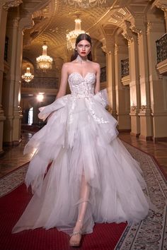 a woman in a white dress standing on a red carpet with chandelier hanging from the ceiling