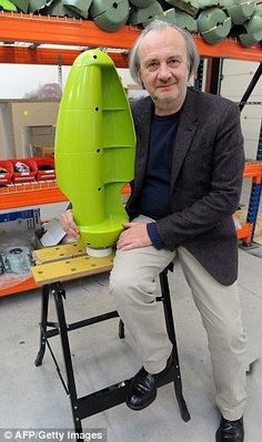 a man sitting in front of a green object on top of a wooden table next to shelves