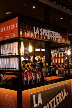 a small bar with lots of bottles on the counter and people sitting at tables behind it