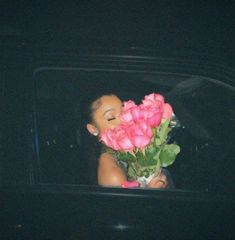 a woman is holding pink roses in her hand and looking out the window at the street