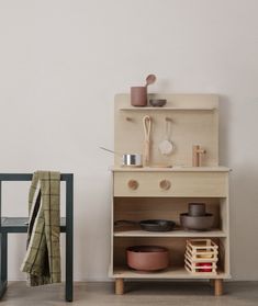 a small wooden cabinet with pots and pans on it next to a stool in front of a white wall