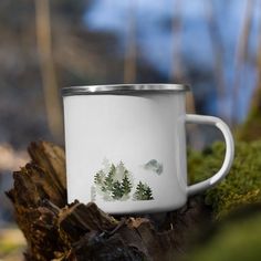 a white coffee cup sitting on top of a moss covered tree stump with trees in the background