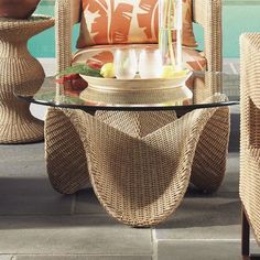 a glass table sitting next to a chair with orange pillows on top of it near a swimming pool