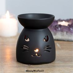 a black cat shaped candle holder sitting on top of a wooden table next to a lit candle