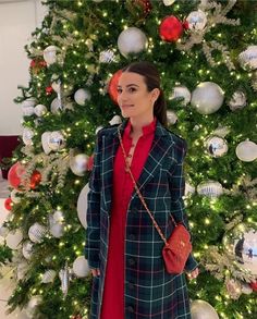 a woman standing in front of a christmas tree wearing a red dress and black coat