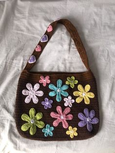 a crocheted purse with multicolored flowers and hearts on the handle is laying on a white sheet