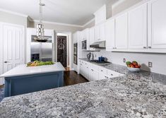 a large kitchen with marble counter tops and white cabinets, along with an island in the middle