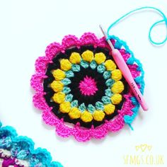 a crochet doily with a pink and yellow flower on it next to a knitting needle