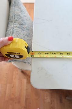 a person holding a tape measure in their left hand and measuring the height of a table