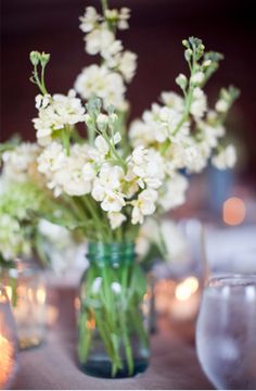 white flowers are in a green vase on a table with candles and wineglasses