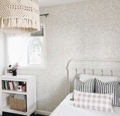 a white bed sitting next to a window in a bedroom under a light hanging from the ceiling