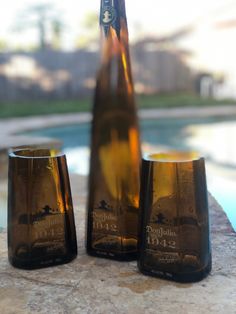 two brown bottles sitting next to each other on top of a stone slab near a swimming pool