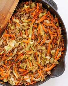 a skillet filled with ground beef, cabbage and carrots next to a wooden spoon