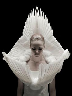 a woman with white hair and wings on her head standing in front of a black background