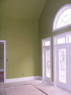 an empty room with green walls and white trim on the door, windows and floor