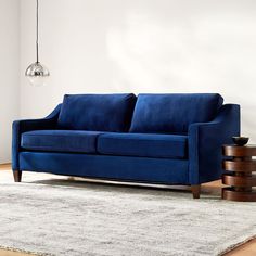 a blue couch sitting on top of a wooden floor next to a table and lamp