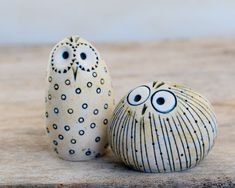 two ceramic owls sitting next to each other on top of a wooden table with eyes painted on them