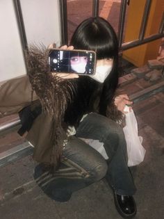 a woman is taking a selfie with her cell phone while sitting on the sidewalk